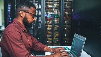 Shot of an male IT technician in a server room and using a laptop 