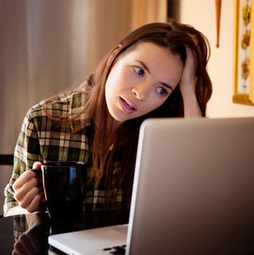 Woman coffee mug looking at laptop computer while sitting at home
