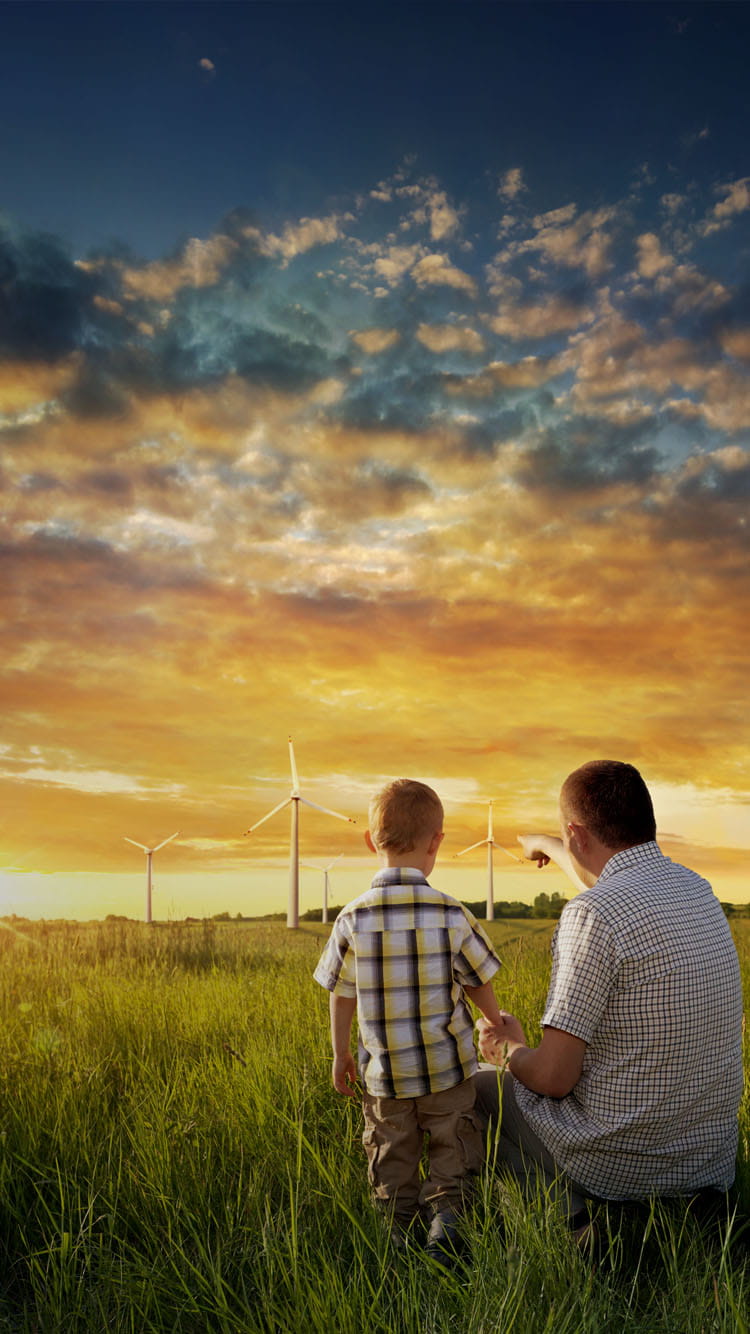 father shows son some wind turbines in a field