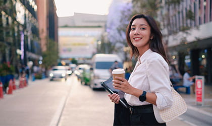 woman crossing the street smiling with coffee in hand