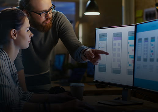 Two people staring at computer code on a dual screen monitor