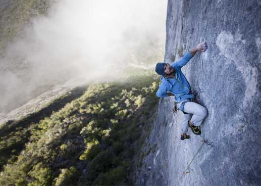 Man climbing side of mountain with one hand