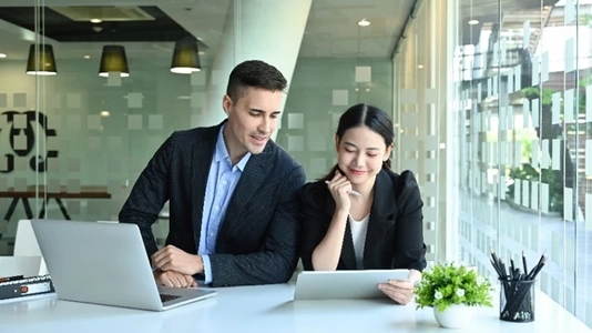 Photo of young office workers sitting together at the working desk surrounded by a computer laptop