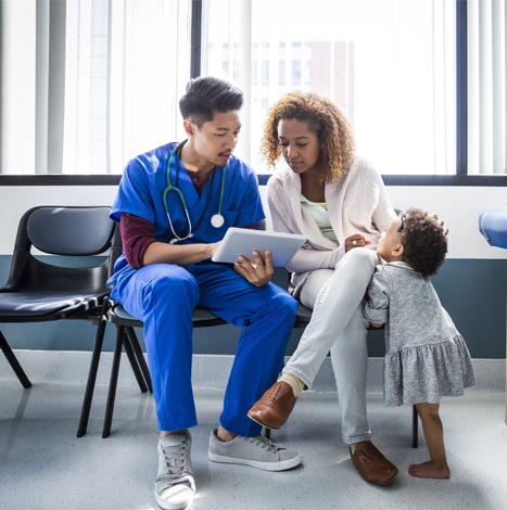 woman and medical professional reviewing tablet together as child looks on