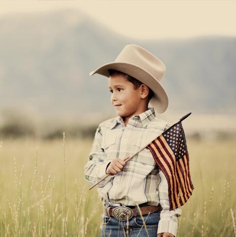 A young cowboy in a field carries an American flag