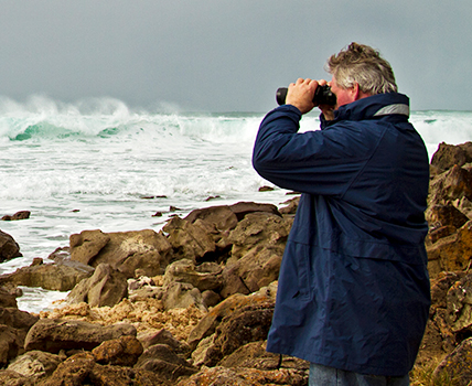 man looing into ocean with binoculars