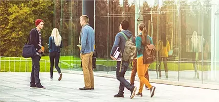 2 students are talking on the street near a transparent building, while others are walking somewhere