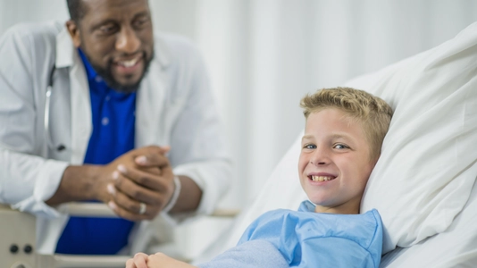 A Caucasian boy is lying in a bed indoors in a hospital room