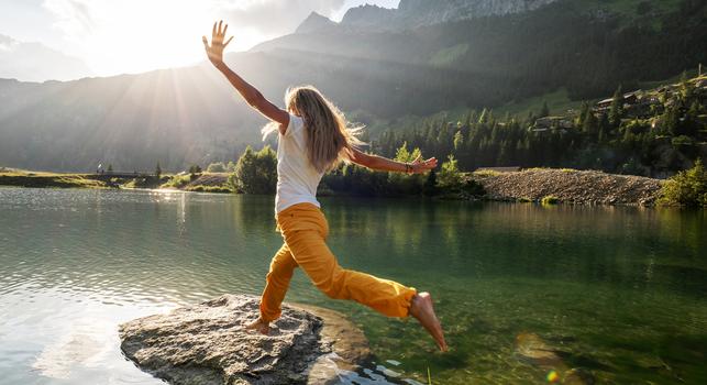 Female hiker jumps from rock to rock above alpine lake