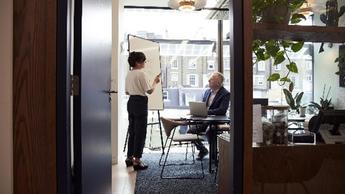 Woman presenting on whiteboard to boss in office