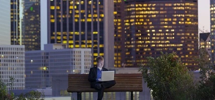 man sitting on bench with laptop and city view behind him