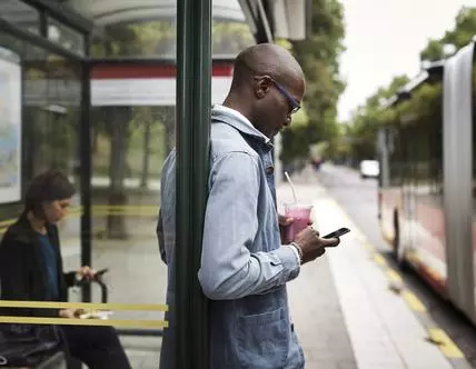 Businessman using smart phone while holding drink at bus stop in city