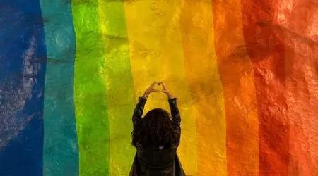 woman holding up hand heart infront of rainbow mural
