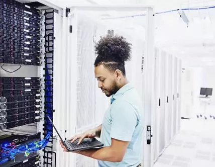 IT professional looking at laptop while working on server in data center