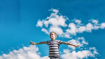 Boy holding an airplane flying it with blue sky and clouds behind him