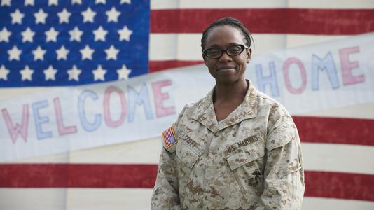 A smiling female soldier stands before the USA flag