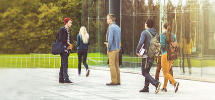 2 students are talking on the street near a transparent building, while others are walking somewhere