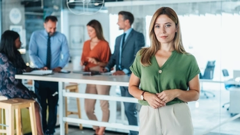 woman looking at camera with group meeting behind her