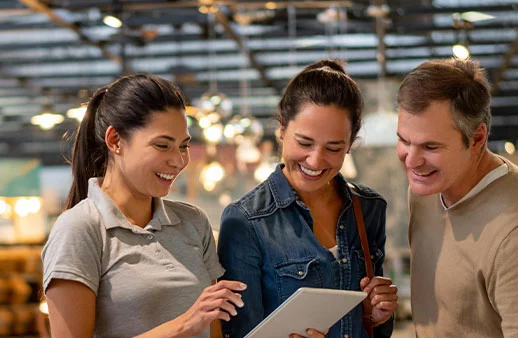 Cheerful sales woman showing a design on tablet to mid adult couple looking for furniture at a home store
