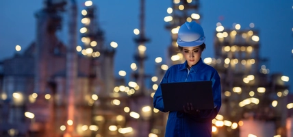 woman in hard hat working on laptop at night with city lights behind her