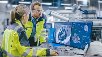 two employees in manufacturing setting reviewing a screen