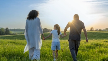 Rear view of parents with daughter walking in dandelion meadow.