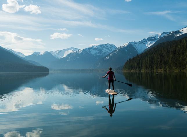 paddle boarder in lake surrounded by mountains