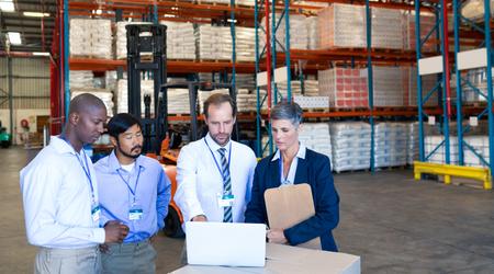 Warehouse staff discussing over laptop in warehouse
