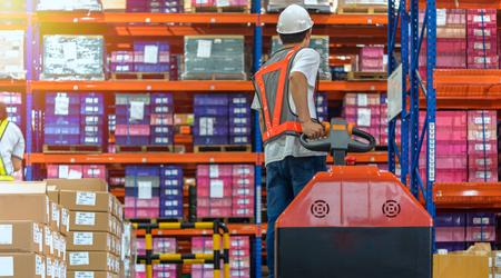 Warehouse worker walking among shelves with hand truck in to large storage room
